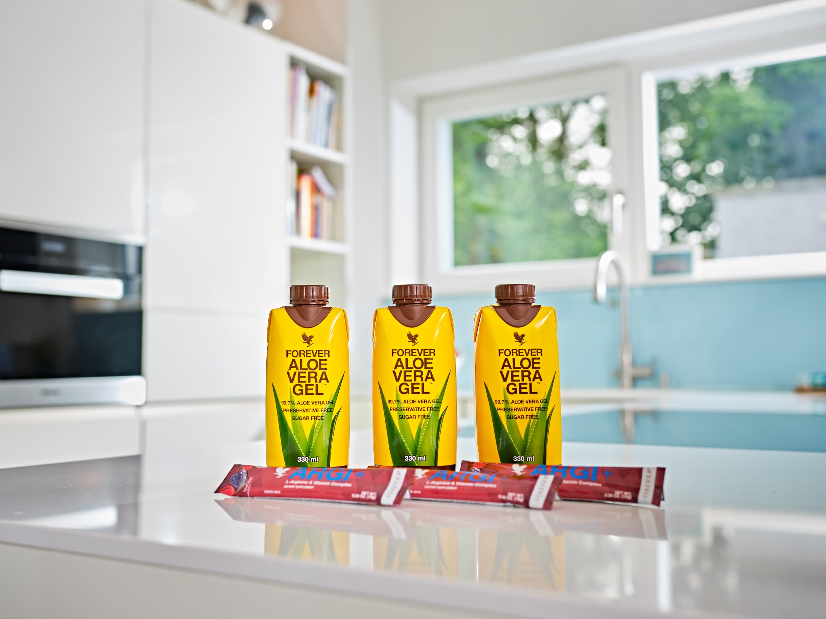 Three 330ml mini Forever Aloe Vera Gel Tetra Paks with ARGI+ on pristine modern kitchen counter